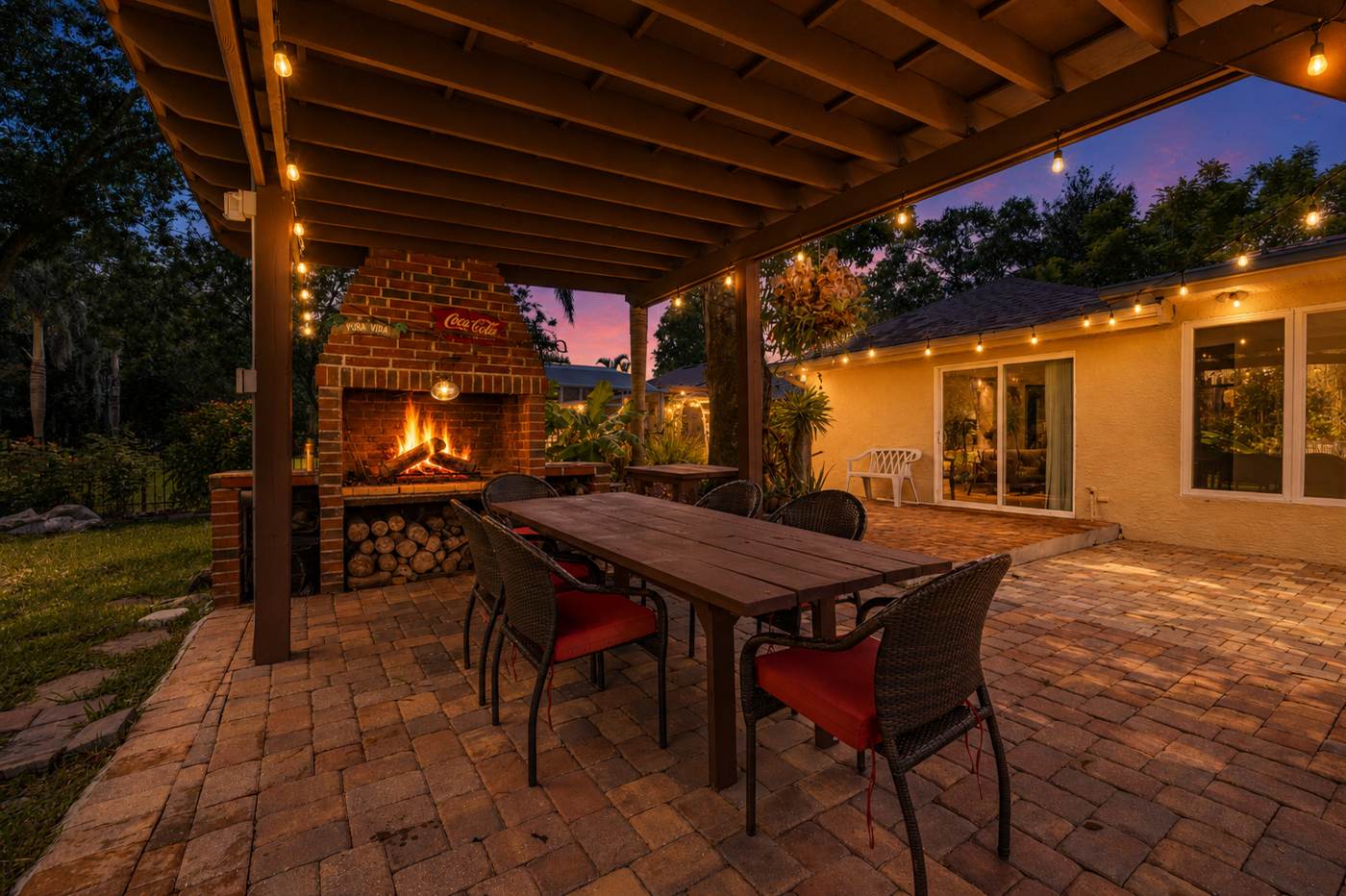 Covered pergola with Argentine-style wood-fire grill and paver patio at dusk at 3625 Waters Edge Dr, Belle Isle Florida